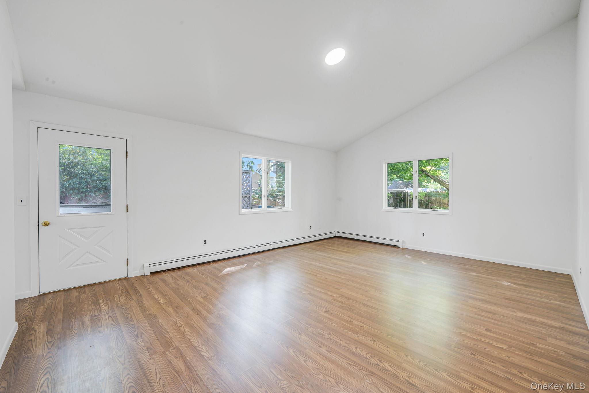 60 Hawthorne Road Rocky Point, NY 11778 - Photo 8 of 23 Empty room featuring plenty of natural light, light wood-style flooring, a baseboard heating unit, recessed lighting, and high vaulted ceiling
