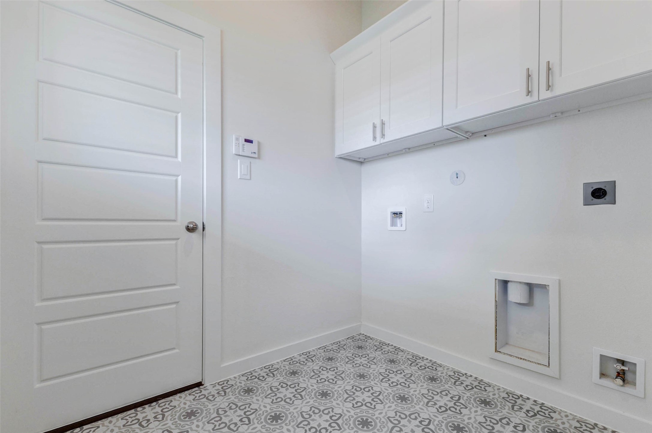 6467 Escondido Drive Rosharon, TX 77583 - Photo 27 of 32 Utility room with patterned tile flooring, washer and dryer hookups, upper storage cabinets, exterior-style door, and wall-mounted thermostat nearby. This dedicated laundry space offers practical function with room for appliances, cleaning supplies, and household storage while keeping laundry conveniently located inside the home.