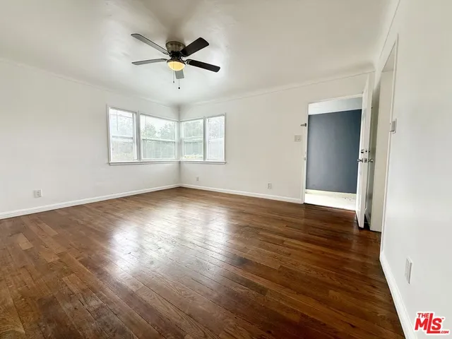 an empty room with wooden floor chandelier fan and windows