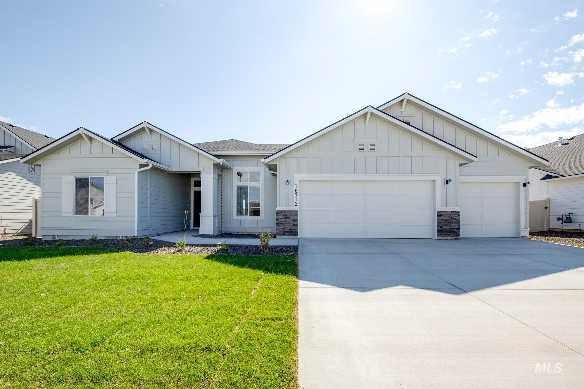 View of front of home with board and batten siding, an attached garage, a front yard, driveway, and a shingled roof