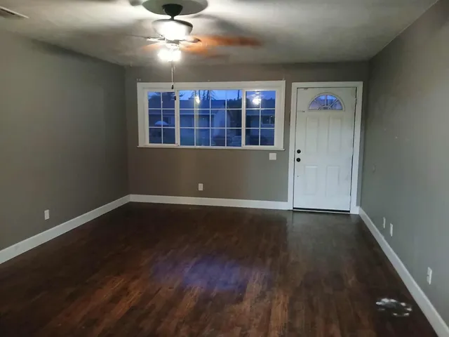 a view of an empty room with wooden floor and a window