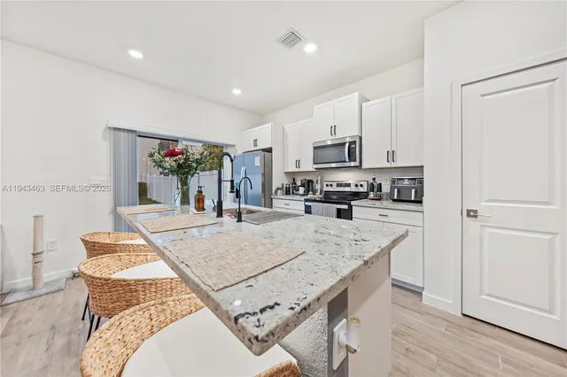 a large kitchen with kitchen island a stove a sink a refrigerator and white cabinets with wooden floor