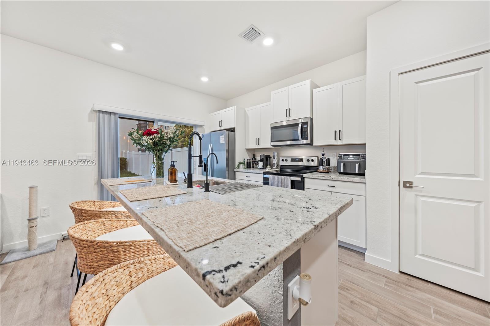 818 Southeast 17 Street, Unit 818 Homestead, FL 33034 - Photo 2 of 36 a large kitchen with kitchen island a stove a sink a refrigerator and white cabinets with wooden floor