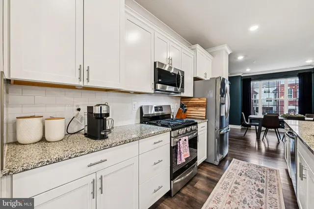 a kitchen with stainless steel appliances granite countertop a stove top oven a sink a dining table and chairs with wooden floor