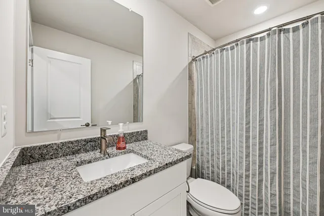 a bathroom with a granite countertop sink vanity mirror and toilet