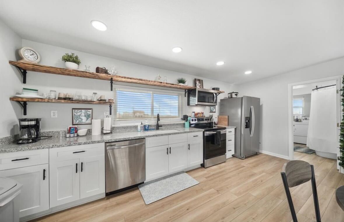 a kitchen with stainless steel appliances granite countertop a refrigerator a sink dishwasher a stove and white cabinets with wooden floor