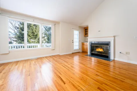 a view of an empty room with wooden floor fire place and a window