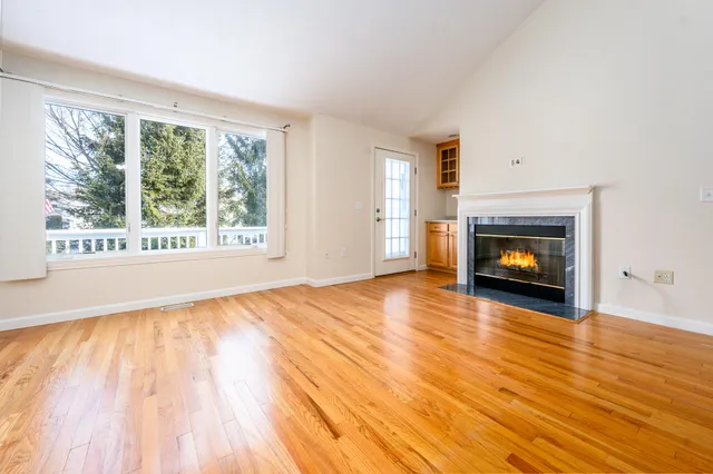 a view of an empty room with wooden floor fire place and a window