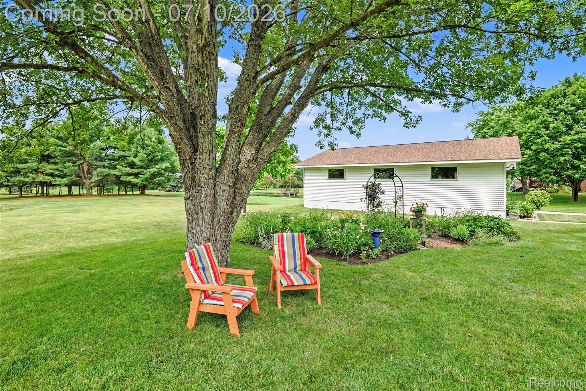 2180 Hurst Road St. Clair, MI 48079 - Photo 31 of 39 Expansive green lawn with a mature shade tree, a perennial garden bed, and a detached outbuilding featuring a brown shingle roof and white siding