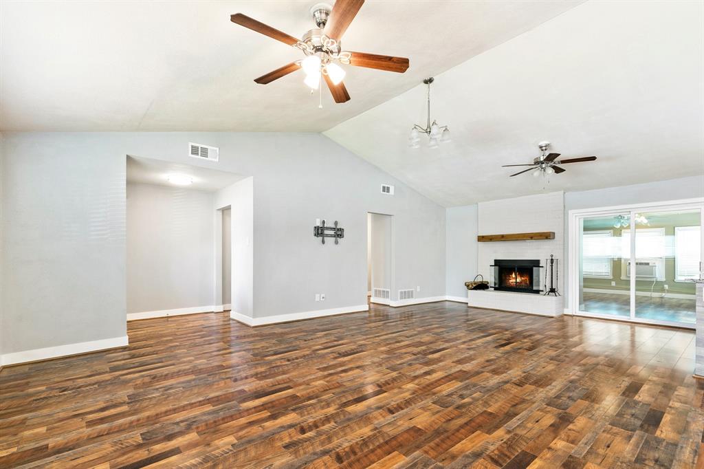 909 North Dove Road Grapevine, TX 76051 - Photo 6 of 30 Spacious living area featuring wood-finish flooring, a vaulted ceiling with multiple ceiling fans, and a white brick fireplace with a wood mantel