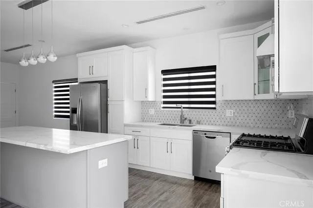 a kitchen with stainless steel appliances a sink dishwasher a stove a refrigerator with white cabinets and wooden floor