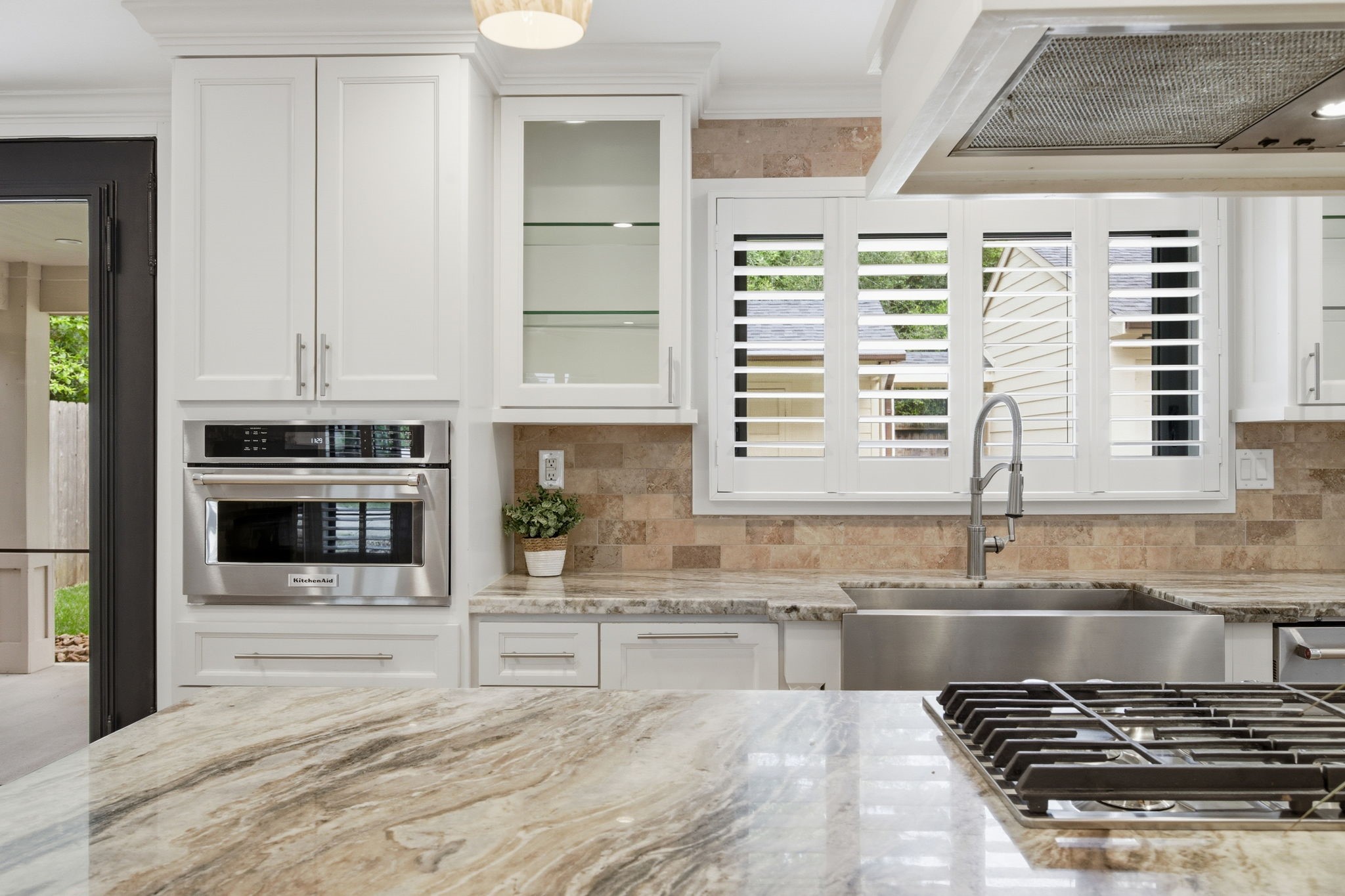 14 Ridgeline Court Spring, TX 77381 - Photo 16 of 40 Another angle of this kitchen featuring the white cabinetry, stainless steel appliances, a large farmhouse sink, and gas cooktop in the island w/breakfast bar. Natural light pours in through the shutters while providing a view of the lush backyard