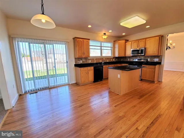 a kitchen with stainless steel appliances granite countertop wooden floors and view of living room