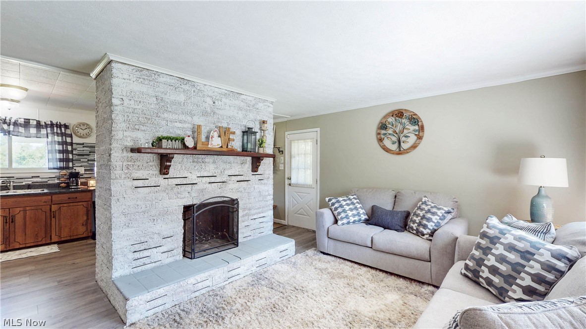 3659 Morrow Road Kent, OH 44240 - Photo 6 of 39 Exposed white-painted brick fireplace with mantel and hearth, featuring wood-finish flooring, light neutral-toned walls, and a recessed kitchen area with dark countertops and wood cabinetry
