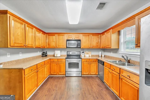 a kitchen with stainless steel appliances granite countertop wooden cabinets a sink dishwasher a stove and a refrigerator with wooden floor