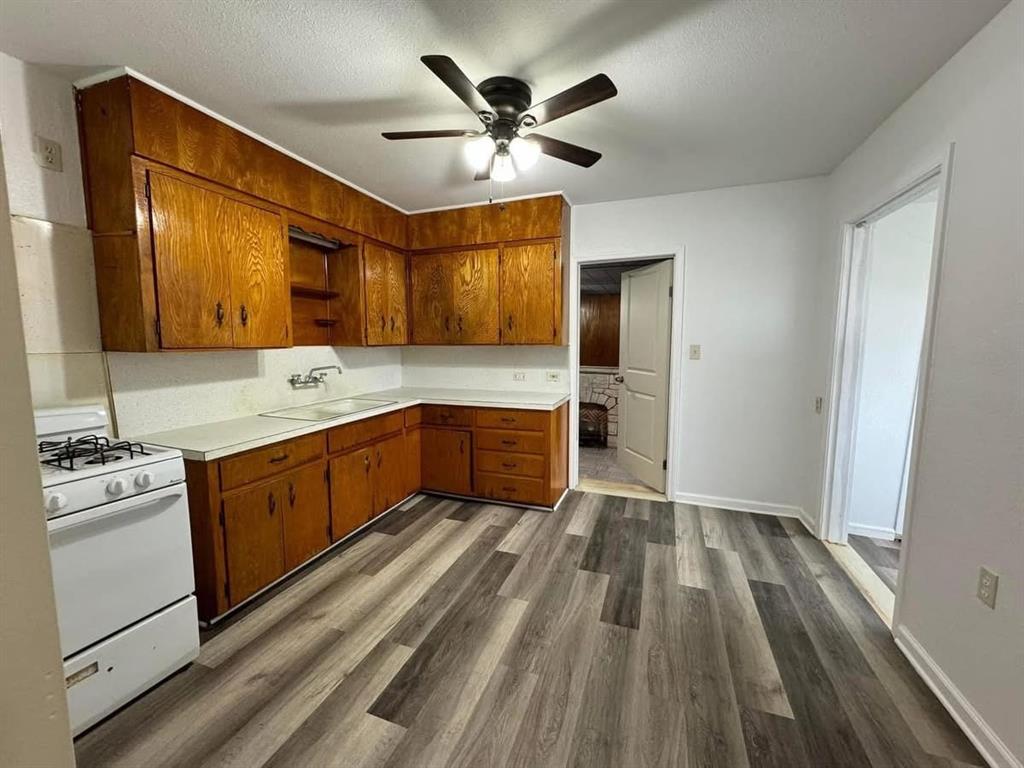 4393 Old Dallas Road Elm Mott, TX 76640 - Photo 10 of 19 Kitchen featuring white gas stove, a ceiling fan, brown cabinetry, light countertops, and dark wood finished floors
