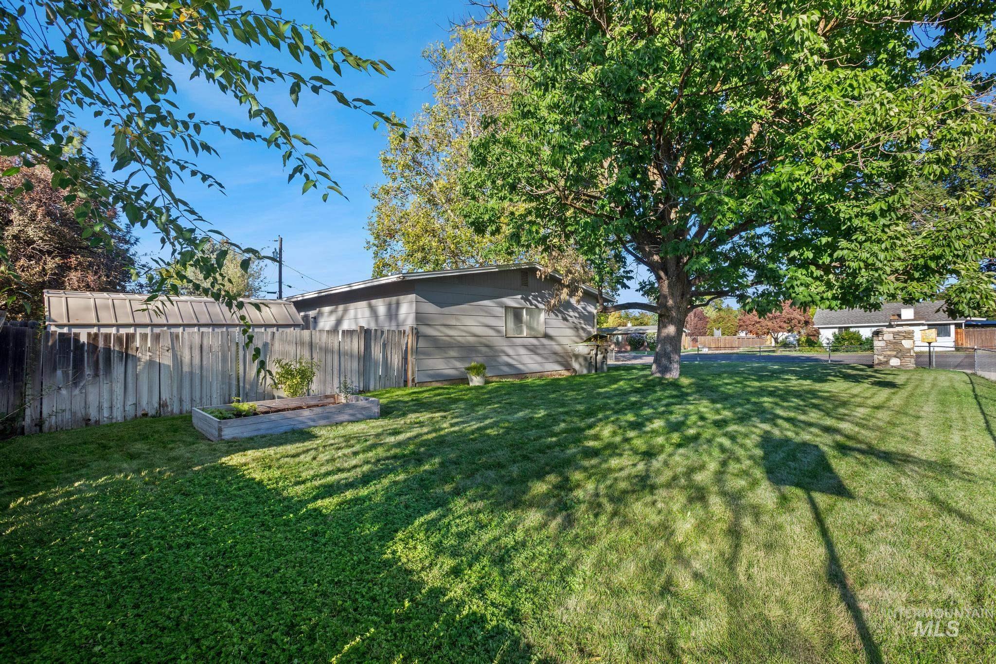2037 South Curtis Road Boise, ID 83705 - Photo 32 of 32 Expansive grass area with a mature tree, wood fencing, and a raised garden bed
