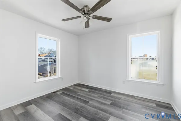 an empty room with wooden floor windows and fan