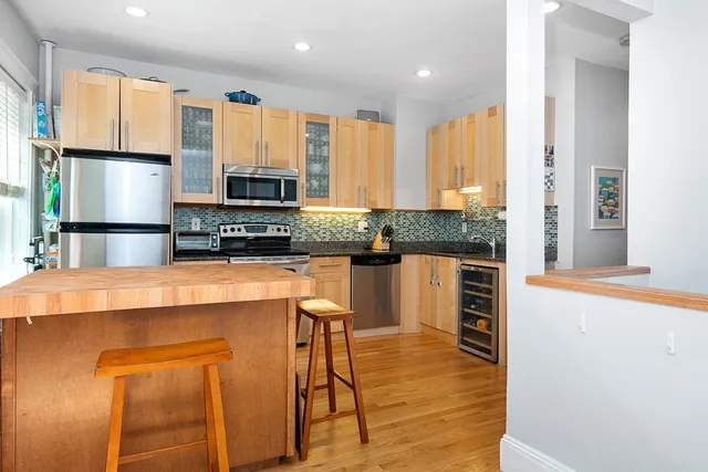 a kitchen with stainless steel appliances kitchen island granite countertop a refrigerator a stove a microwave oven with white cabinets and wooden floor