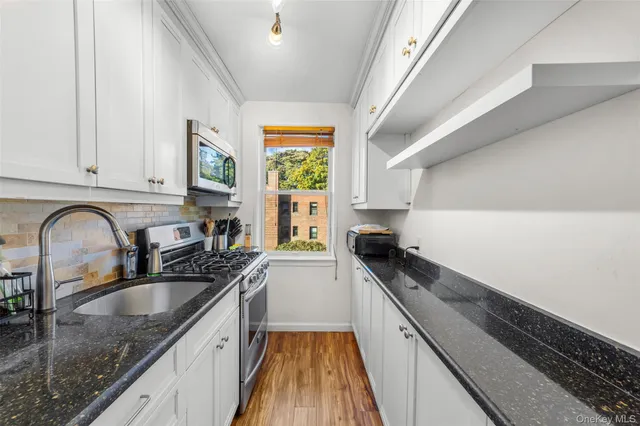 a kitchen with granite countertop stainless steel appliances a sink a stove cabinets counter space and a window