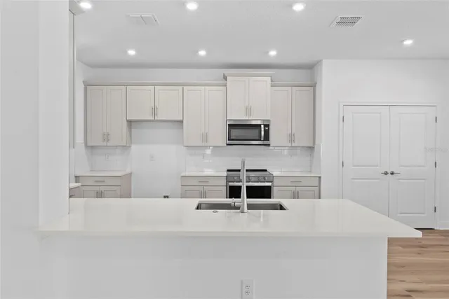 a kitchen with stainless steel appliances a stove top oven a sink a refrigerator and white cabinets