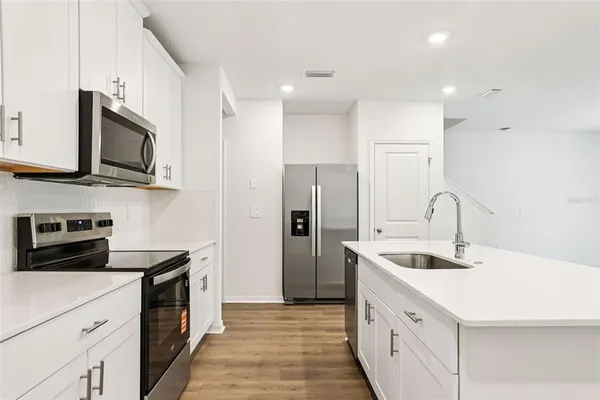 a kitchen with stainless steel appliances granite countertop a stove top oven a refrigerator and white cabinets with wooden floor