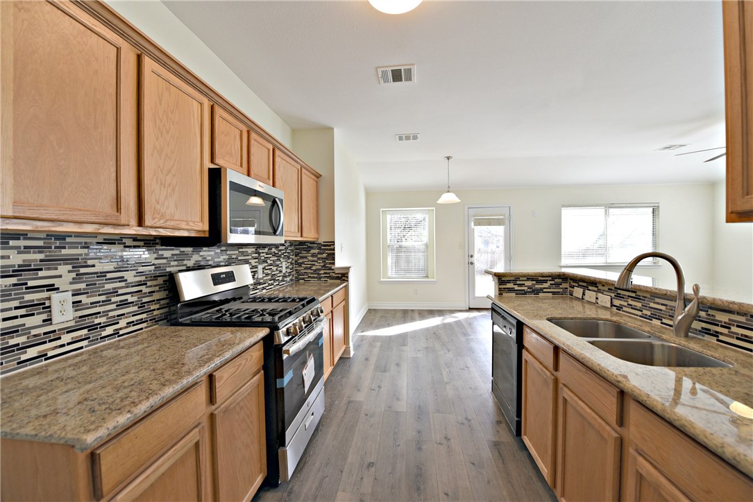 3665 Spring Canyon Trail Round Rock, TX 78681 - Photo 10 of 21 a kitchen with stainless steel appliances granite countertop a stove a sink dishwasher and a microwave oven with wooden floor