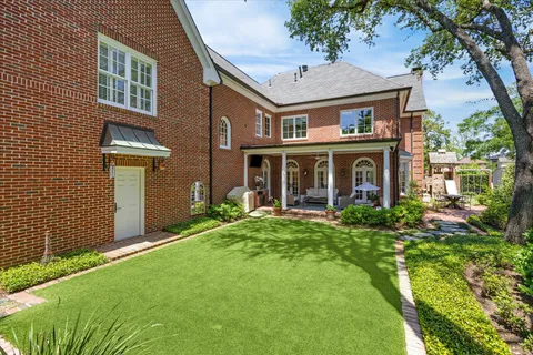 a view of a brick house with a yard plants and large tree