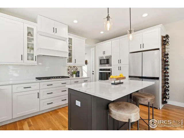 a kitchen with stainless steel appliances kitchen island granite countertop a stove a sink dishwasher and white cabinets with wooden floor