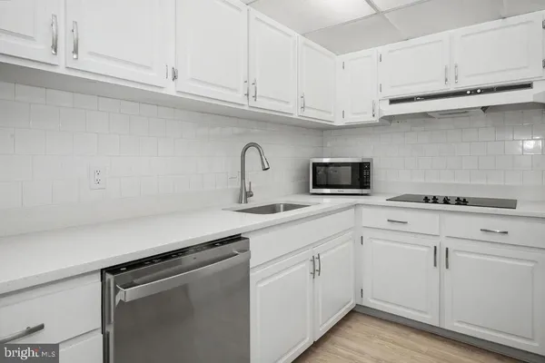 a kitchen with stainless steel appliances granite countertop a sink dishwasher a stove and white cabinets with wooden floor