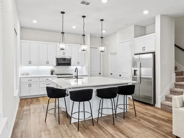 a kitchen with stainless steel appliances kitchen island a refrigerator a sink dishwasher and a stove with wooden floor