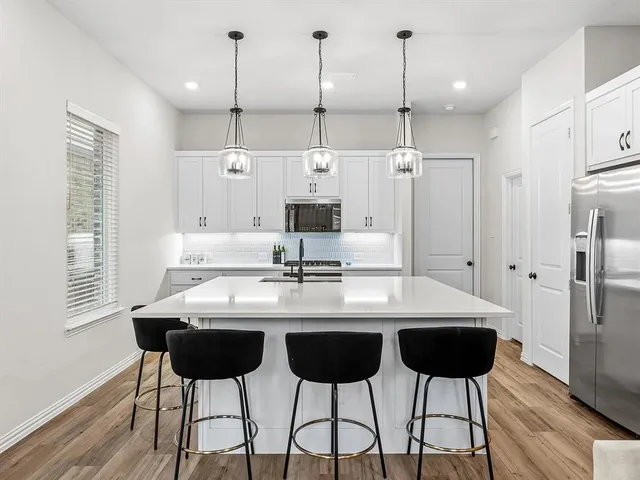 a kitchen with stainless steel appliances granite countertop a dining table chairs and white cabinets