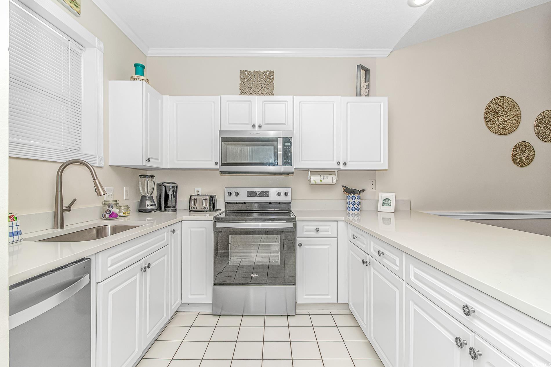 4647 Wild Iris Drive, Unit 303 Myrtle Beach, SC 29577 - Photo 7 of 29 Kitchen with appliances with stainless steel finishes, white cabinets, crown molding, light stone countertops, and light tile patterned flooring