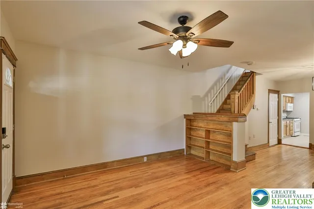 a view of an empty room with wooden floor and a ceiling fan