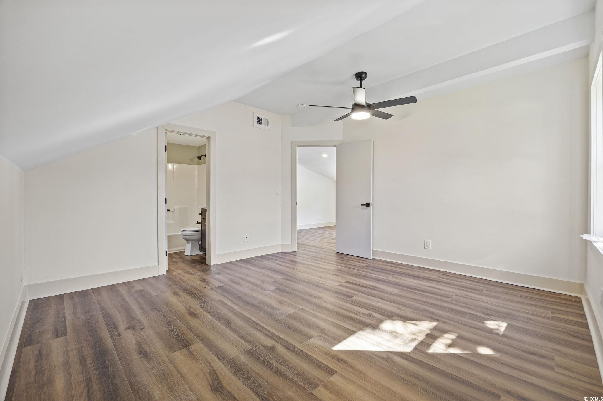 513 Plantation Drive Surfside Beach, SC 29575 - Photo 25 of 44 Upstairs suite bedroom featuring wood-finished LVP flooring, a lofted ceiling, ceiling fan, and a private ensuite bath—offering comfort and style in a quiet retreat.