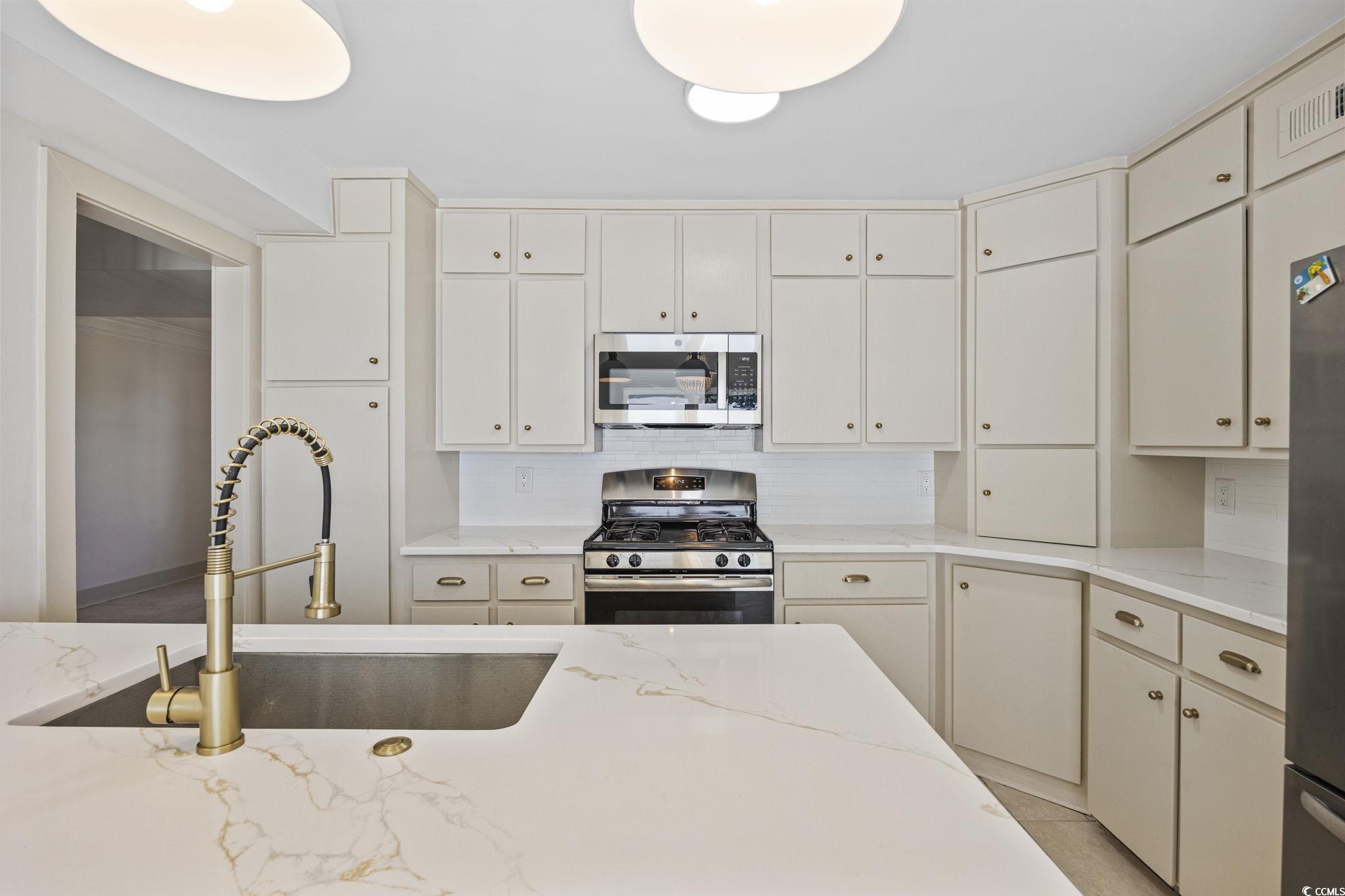 513 Plantation Drive Surfside Beach, SC 29575 - Photo 6 of 44 Beautifully remodeled kitchen featuring stainless steel appliances, cream cabinetry, light quartz stone countertops, polished brass hardware, and a stylish decorative backsplash.