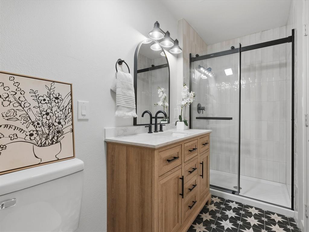 289 County Road 4655 Rhome, TX 76078 - Photo 17 of 34 Upstair Bathroom featuring a wood-finish vanity with a white countertop, black hardware, an arched mirror, and a black-framed glass shower enclosure