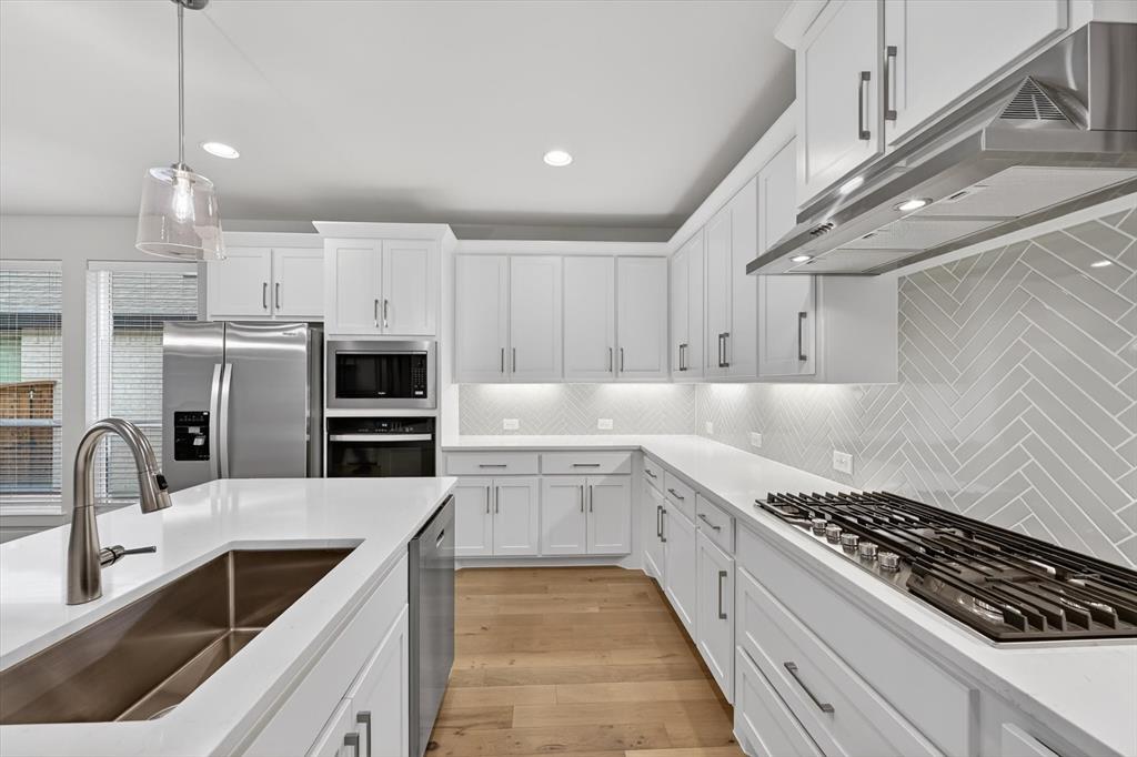 4123 Windy Point Court Oak Point, TX 75068 - Photo 15 of 29 Contemporary kitchen featuring white cabinetry, light countertops, wood-finish flooring, a herringbone-patterned tile backsplash, and stainless steel appliances including a gas range, built-in microwave, and oven