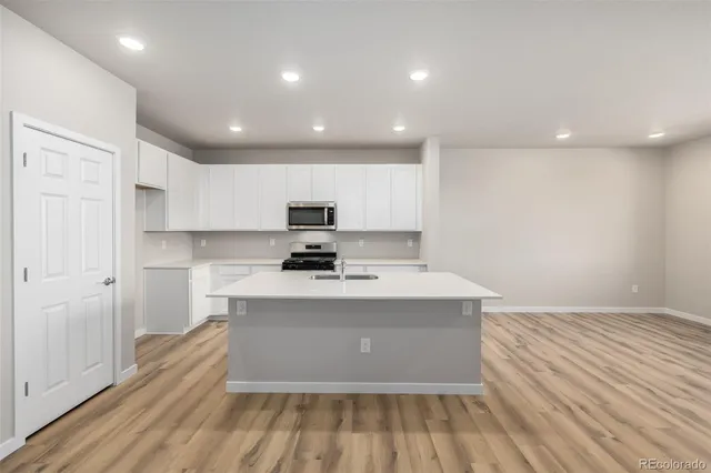a view of a kitchen with kitchen island a sink wooden floor and stainless steel appliances
