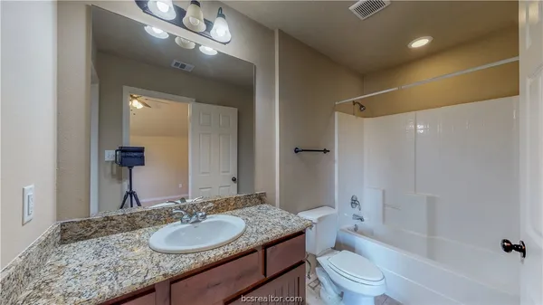 a bathroom with a granite countertop sink a toilet a mirror and shower