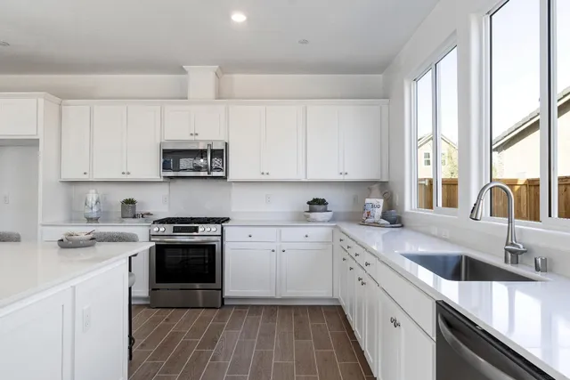 a kitchen with stainless steel appliances granite countertop a sink dishwasher a stove top oven a refrigerator with white cabinets and wooden floor