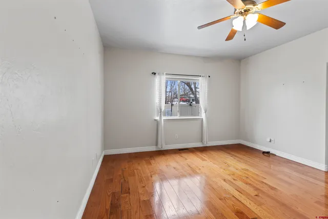 an empty room with wooden floor chandelier fan and windows