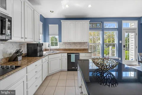 a kitchen with granite countertop white cabinets stainless steel appliances a sink and a large window