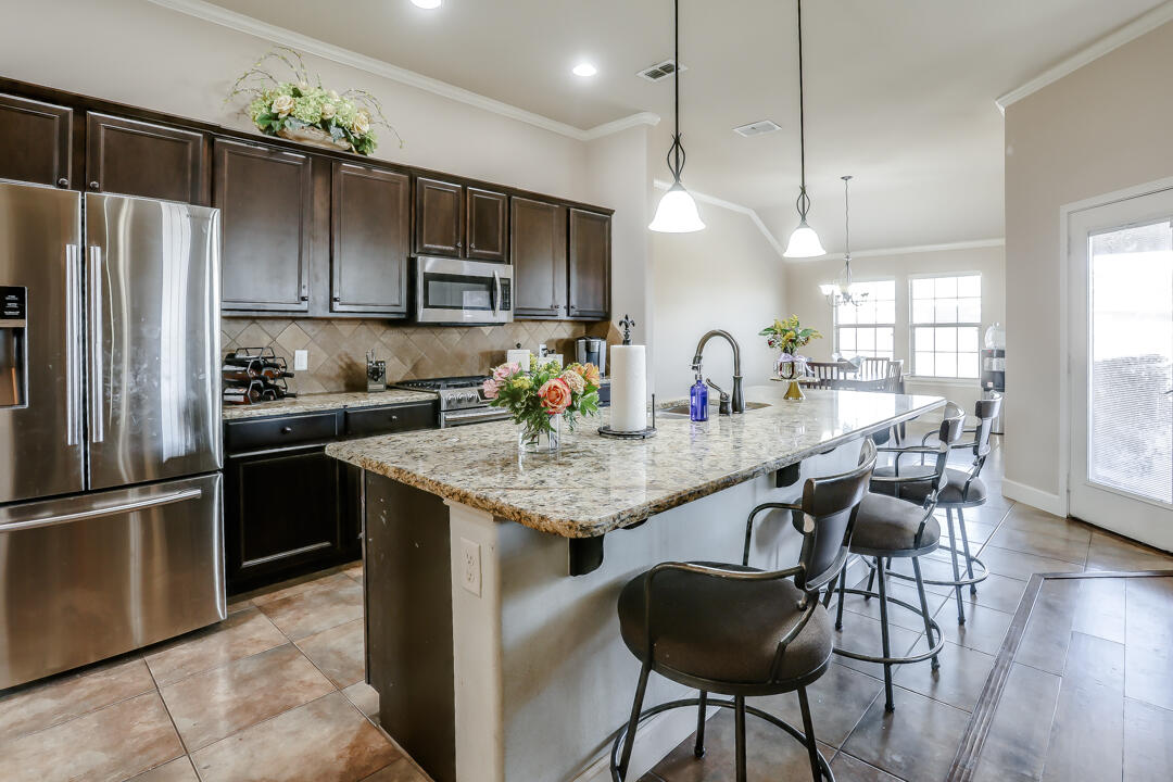 6502 71st Street Lubbock, TX 79424 - Photo 7 of 21 a kitchen with granite countertop kitchen island stainless steel appliances a refrigerator a sink a center island cabinets and a counter top space