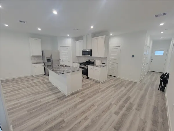 a large white kitchen with kitchen island a sink a stove a refrigerator and white cabinets with wooden floor