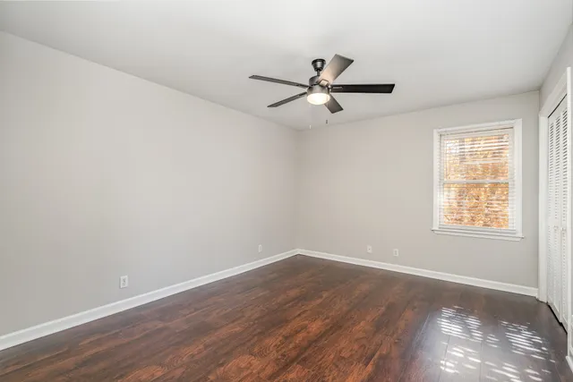 an empty room with wooden floor fan and windows