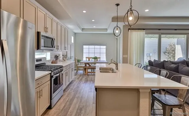 a open kitchen with stainless steel appliances granite countertop a stove refrigerator a sink dishwasher a dining table and chairs with wooden floor