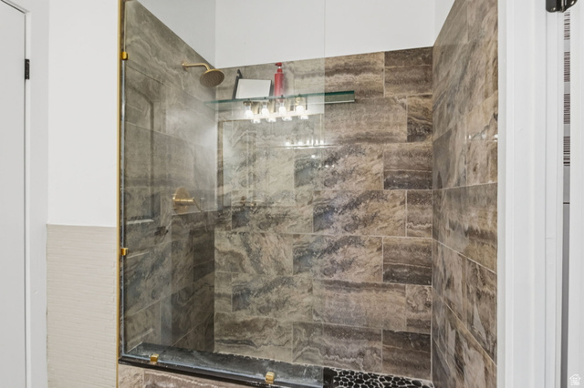 4270 River Road Oakley, UT 84055 - Photo 31 of 46 Walk-in shower featuring glass enclosure with brass-finish hardware, large format stone tile walls, a pebble-finish floor, and a built-in glass shelf