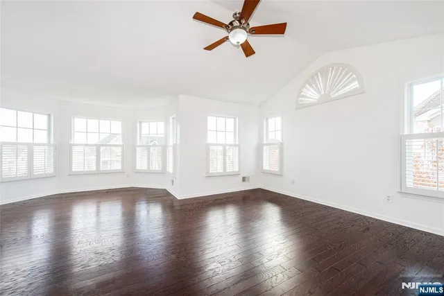 an empty room with wooden floor fan and windows