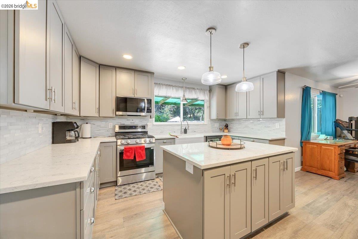 8733 Fraguero Road Sonora, CA 95370 - Photo 28 of 73 Modern kitchen featuring light gray cabinetry, stainless steel appliances, a center island with pendant lighting, white countertops, and wood-finish flooring